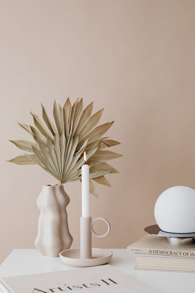 A minimalist arrangement featuring a vase with dry palm leaves and a candle.